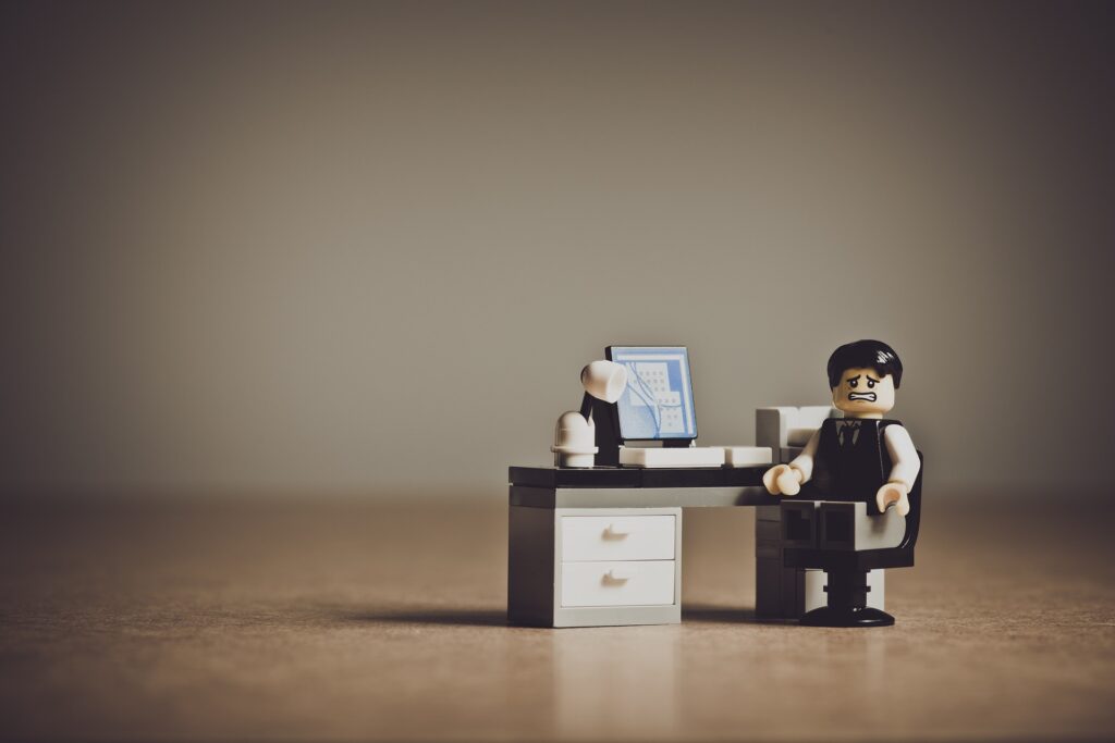 Verzweifelt schauende Lego-Figur sitzt an einem Schreibtisch vor PC (alles aus Lego)