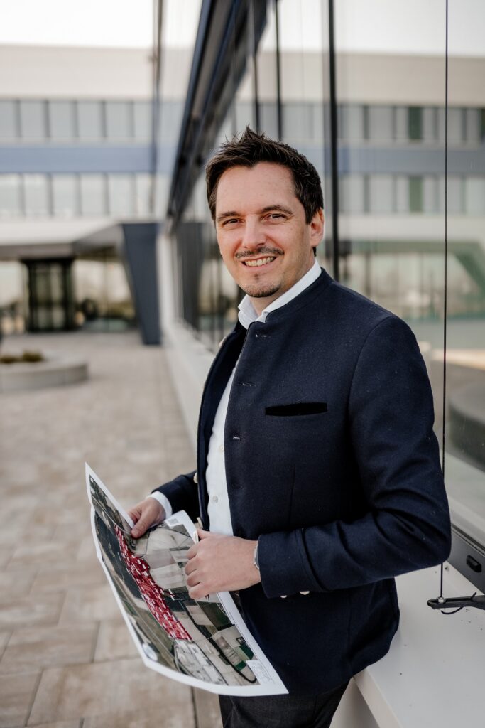 Vorstand Johannes Hofner vor Gebäude mit Plan in der Hand